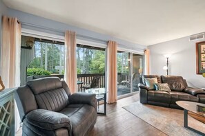 A spacious living room with a leather sofa, a glass coffee table, and a balcony with outdoor furniture. - Birdie Bungalow - Sleeps 8 - Prime Location (Pinehurst)