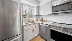 A modern kitchen with stainless steel appliances, white cabinetry, and a window with blinds. - Birdie Bungalow - Sleeps 8 - Prime Location (Pinehurst)
