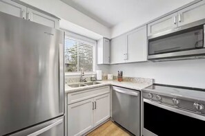 A modern kitchen with stainless steel appliances, white cabinetry, and a window with blinds. - Birdie Bungalow - Sleeps 8 - Prime Location (Pinehurst)
