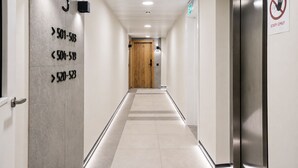 Moderni hotellikäytävä, jossa on numeroituja ovia, käytävän päässä puuovi ja kyltti, jossa lukee: «Vain henkilökunnan käyttöön».