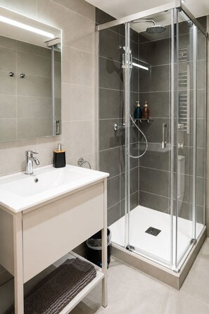 A modern bathroom with a glass-enclosed shower, a white sink, and a mirror above it.