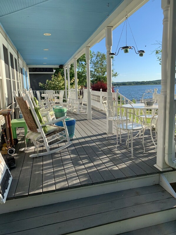 A covered deck with white chairs and tables, overlooking a body of water.