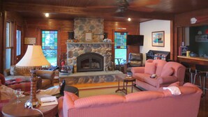 A cozy living room with a stone fireplace, a ceiling fan, and a television mounted on the wall.