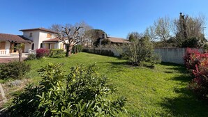 Um imóvel residencial com gramado bem cuidado, uma grande árvore e um muro de pedra.