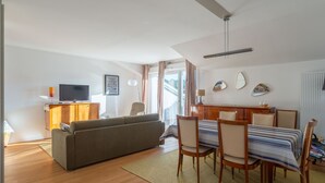 Un salon comprenant un canapé, un téléviseur, un meuble en bois, une table à manger avec des chaises, et une vue à travers une porte vitrée.