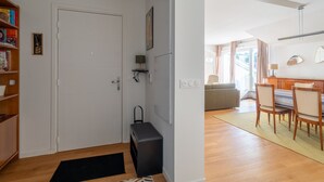Un intérieur moderne avec une porte blanche, un meuble de rangement noir, un coin repas avec une table et des chaises, et une bibliothèque remplie de livres et d’objets décoratifs.