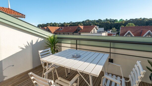 Une terrasse sur le toit, avec une table et des chaises, un pot de fleurs et une vue sur des bâtiments aux toits rouges.