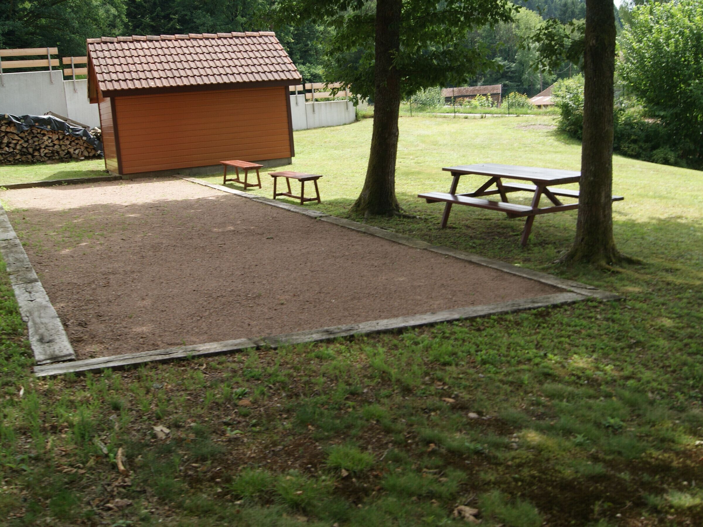 A fenced outdoor area with a wooden shed, picnic tables, and a gravel path.