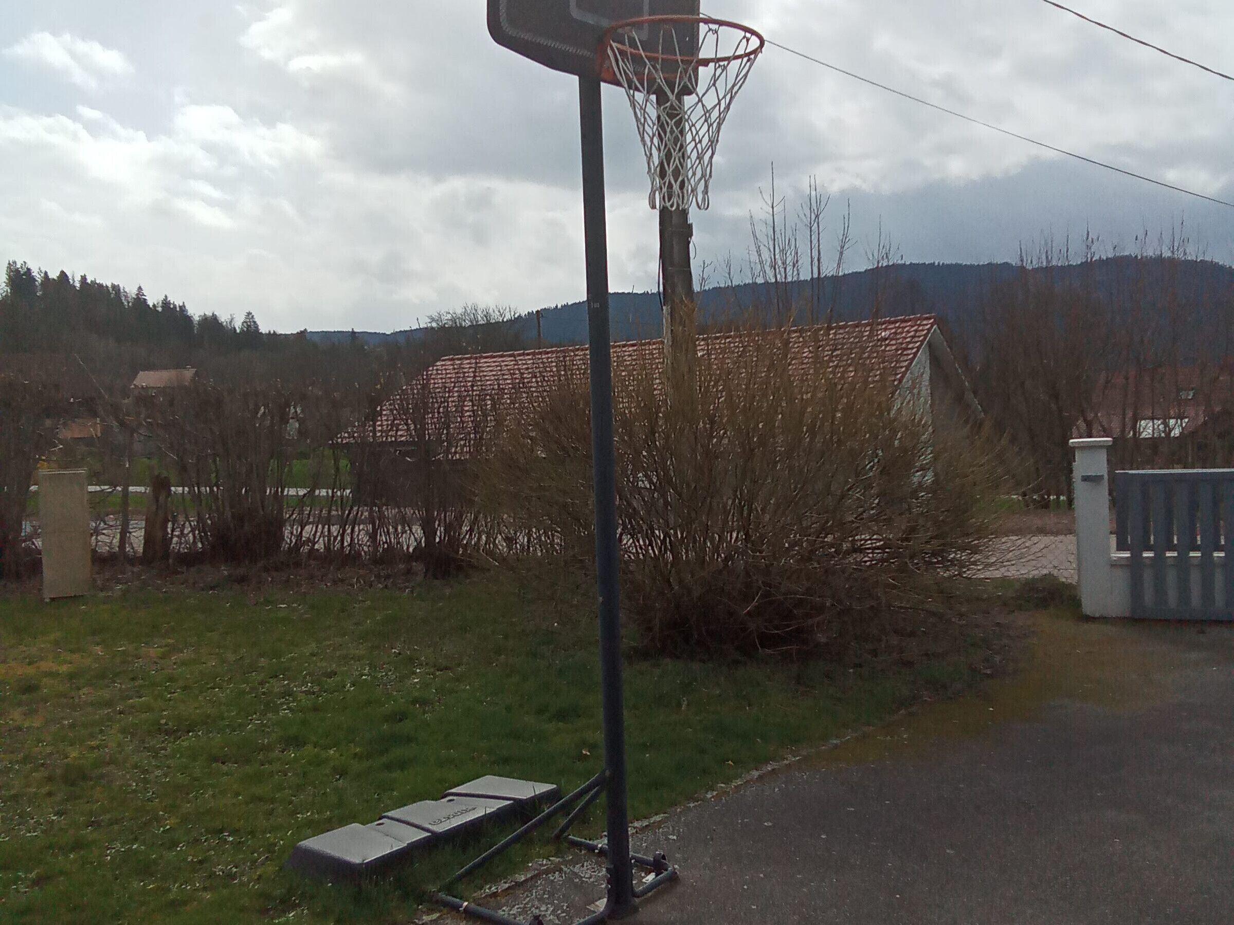 Een basketbalveld met een ring, omringd door gras, een hek en een gebouw op de achtergrond.