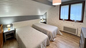 A bedroom with two beds, a nightstand with a lamp, a dresser, and a window with curtains. - Spacious chalet near Gérardmer (Gerbamont)
