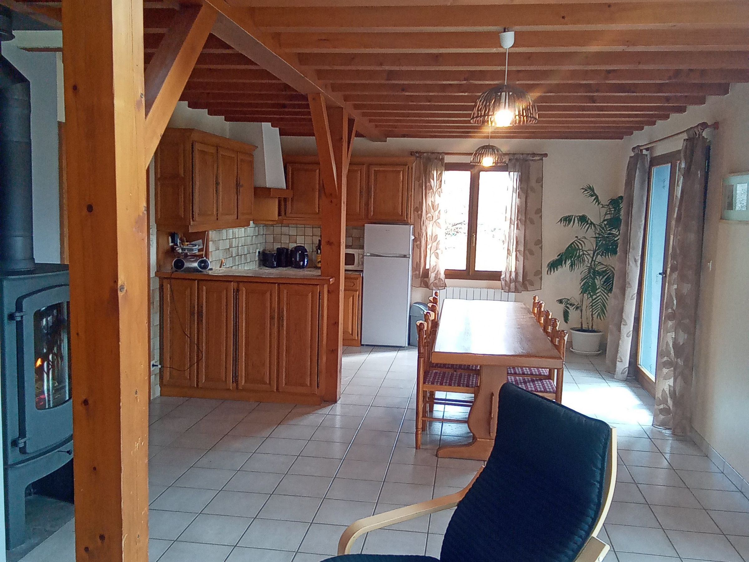 A kitchen with wooden cabinets, a tiled floor, a dining table with chairs, a refrigerator, and a stove.