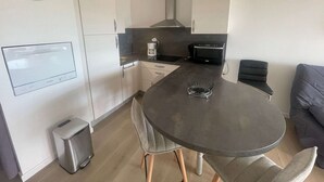 A modern kitchen with a dining table, chairs, a coffee machine, a toaster, and a clock on the wall. - 2-Room Apartment in La Grande-Motte, Near Beach and Shops, Private Parking (La Grande-Motte)