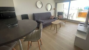A modern living space with a dining table, sofa, chairs, and a TV. - 2-Room Apartment in La Grande-Motte, Near Beach and Shops, Private Parking (La Grande-Motte)