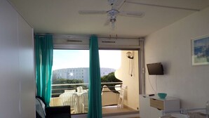 Habitación con sofá, una mesa de comedor, televisor y balcón con vista a edificios.