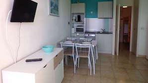 Una cocina compacta con comedor, un televisor montado en la pared y una pequeña mesa con sillas.