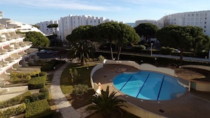 Edificio residencial con piscina, rodeado de vegetación y otros edificios.