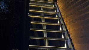 A staircase with a wooden handrail and steps, leading up to a building with a window and a light fixture.