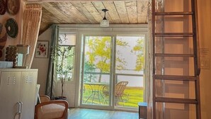 A room with a wooden ceiling, a sliding glass door leading to an outdoor area, a ladder, and a chair.