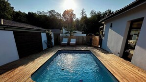 Una piscina rectangular con cubierta de madera, rodeada por un edificio blanco con garaje.