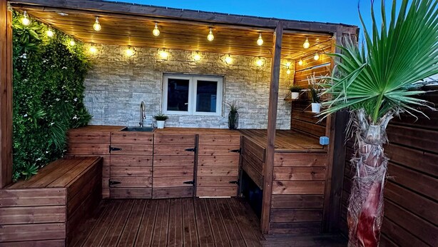 Una terraza de madera con bancos integrados, un muro de piedra y luces colgantes.
