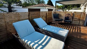 Una terraza de madera con mobiliario de mimbre, incluyendo dos sillones reclinables y una mesita.