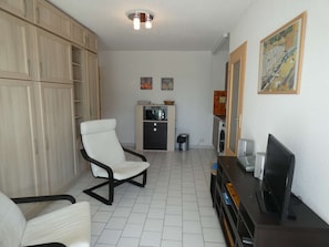 A room with a white chair, a TV, a cabinet, and a microwave. - Studio cabin with pool, air conditioning, garage, 300m from beach (La Grande-Motte)