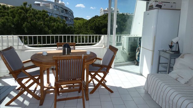 En balkon med et træbord og stole, en sofa og udsigt til bygninger og træer.