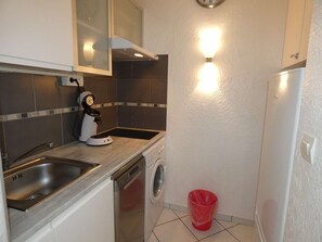 A compact kitchen with a sink, a coffee machine, a washing machine, and a red trash bin. - Sunny 2-Room Apartment with Pool, Near Shops and Beach, Parking Included (La Grande-Motte)