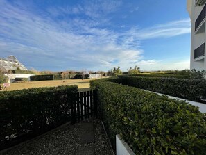 Ein Wohngebiet mit einer gepflegten Hecke, einem befestigten Weg und einem entfernten Blick auf ein modernes Gebäude mit einer markanten Dachkonstruktion.