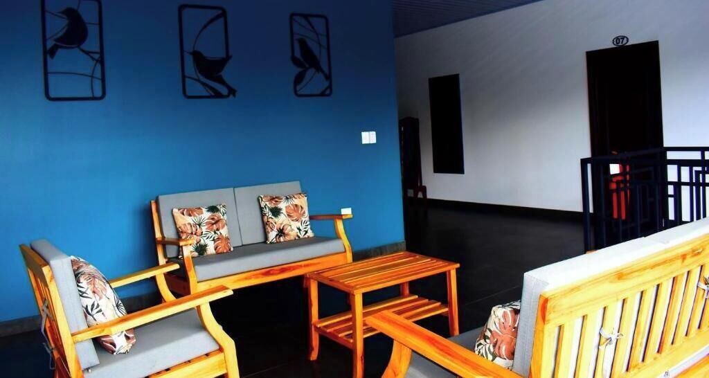 Een kamer met een blauwe wand, een bank met bloemenkussens, een houten tafel en een houten bankje.