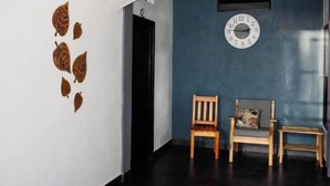 Una habitación con una pared azul oscuro, una pared blanca decorada con hojas, una silla de madera, una mesita y un reloj.