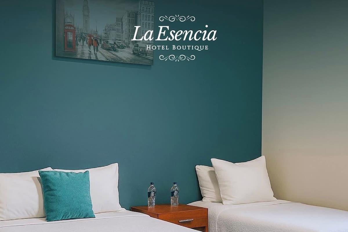 A hotel room with two beds, teal walls, and a cityscape painting.