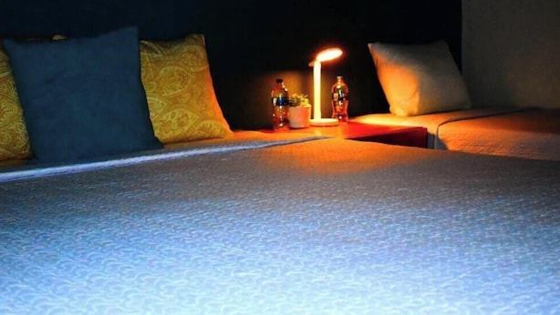 A bed with a patterned bedspread, pillows, a bedside table with a lamp, and bottles. - Hotel Boutique La Esencia  (El Jícaro)