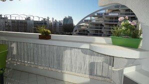 A balcony with a view of a modern building complex, a green plant, and a beige awning. - Charming Studio Steps from the Beach with Parking and Wi-Fi (La Grande-Motte)