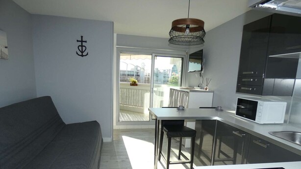 A modern kitchen with a dining area, a sofa, and a view of the outside. - Charming Studio Steps from the Beach with Parking and Wi-Fi (La Grande-Motte)