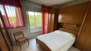 Une chambre à coucher avec un lit, une chaise, une fenêtre avec des rideaux et une vue sur la verdure à l’extérieur.