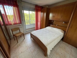 Un dormitorio con cama, una silla, una ventana con cortinas y vista a zonas verdes.