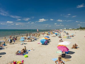 Une plage bondée où les gens se prélassent au soleil et se baignent, et un drapeau flotte sur le rivage.