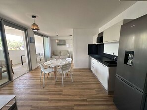 Eine moderne Küche mit einem Edelstahl-Kühlschrank, weißen Schränken und einem Essbereich mit rundem Tisch und Stühlen.