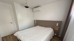 A bedroom with a bed, a door, an air conditioning unit, and a light fixture. - Luxury A/C Apartment Near Beach and Shops - 2 Rooms, Parking, High-Quality Amenities (La Grande-Motte)