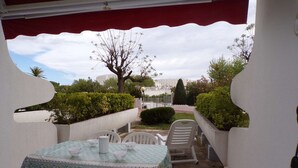 An outdoor patio with a table and chairs, a view of a cityscape, and a red awning. - Cozy Studio with Pool Access, Near Beach and Shops, Sleeps 4, Private Parking (La Grande-Motte)