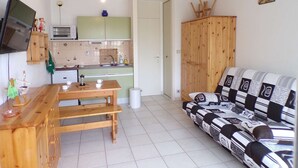 A compact living space with a kitchenette, a dining area with a bench, and a sofa with patterned cushions. - Cozy Studio with Pool Access, Near Beach and Shops, Sleeps 4, Private Parking (La Grande-Motte)