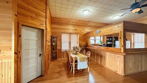 Interior d'una cabana de fusta amb zona de dinar, cuina i barra.
