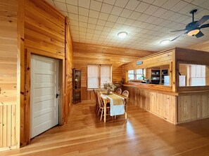 A wooden cabin interior with a dining area, a kitchen, and a bar.