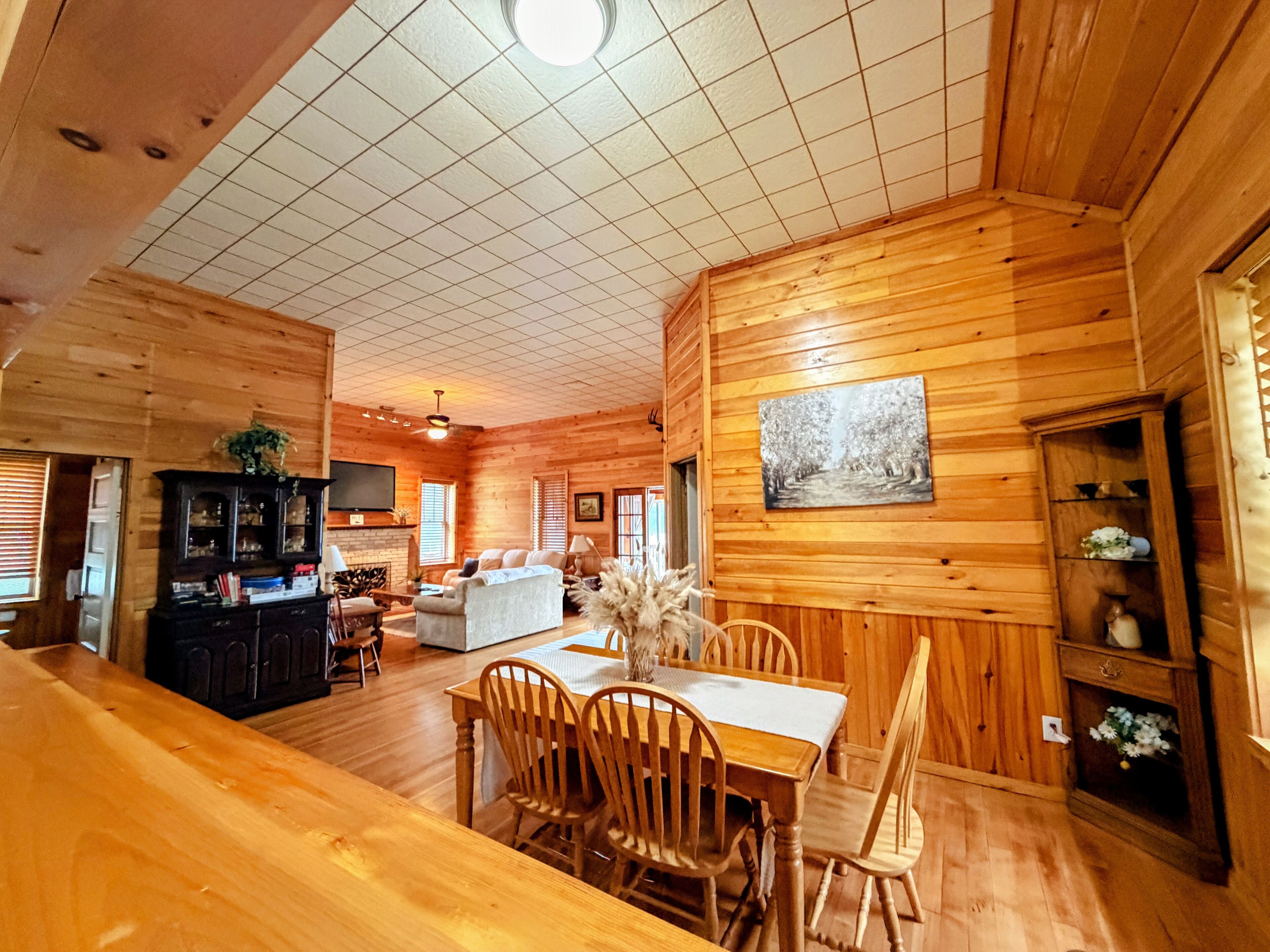 A spacious wooden interior with a dining area, a fireplace, and a television mounted on the wall.