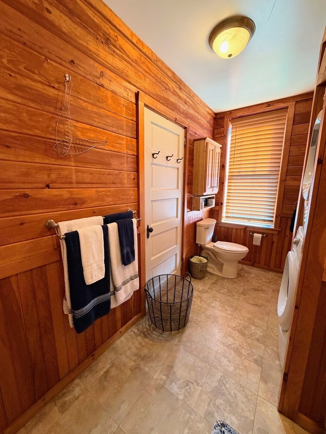Bagno con rivestimento in legno, dotato di water, lavandino e finestra.