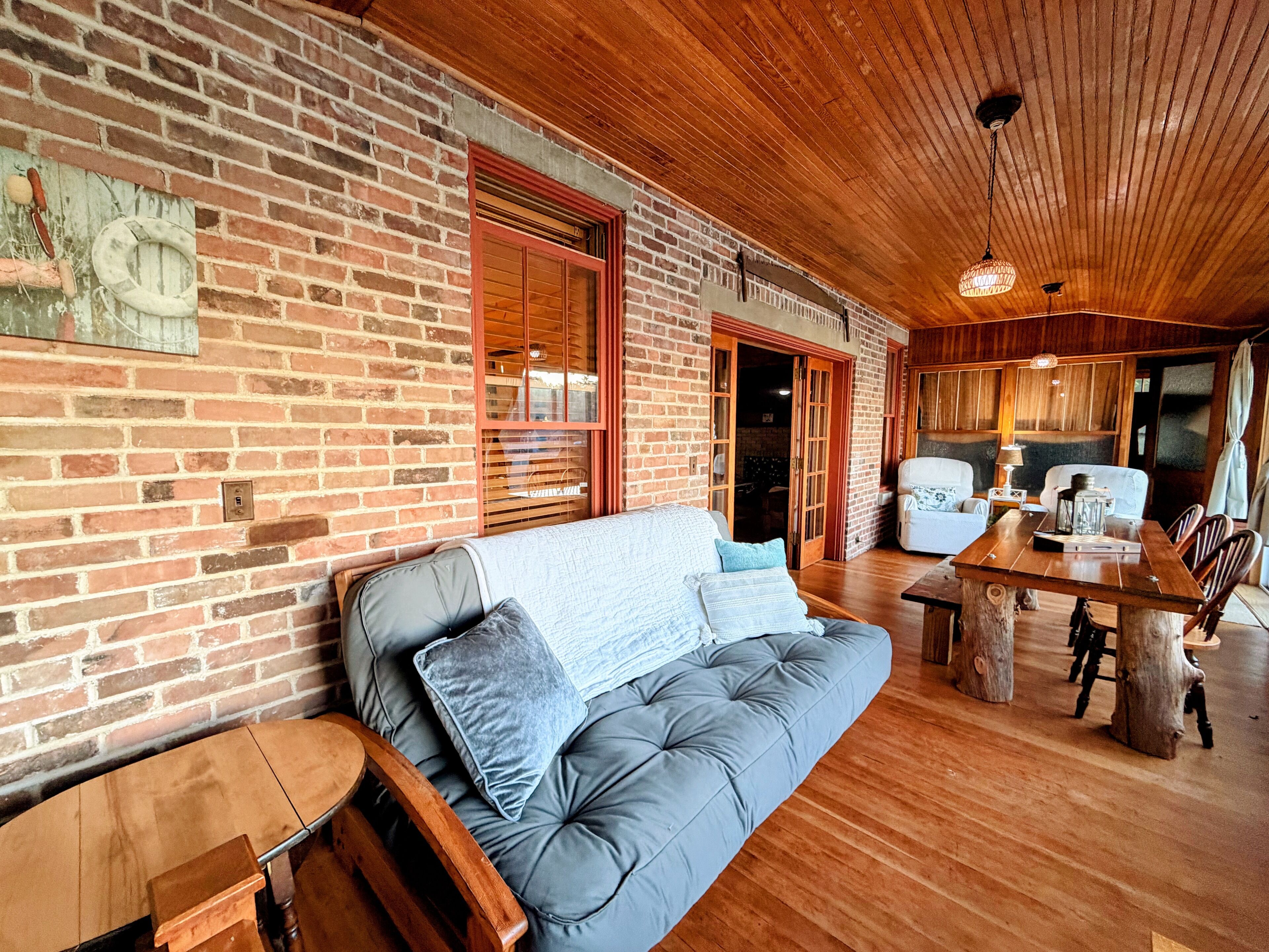 Una habitación acogedora con pared de ladrillo, techo de madera, sofá gris con cojines, una mesa de madera y una silla.