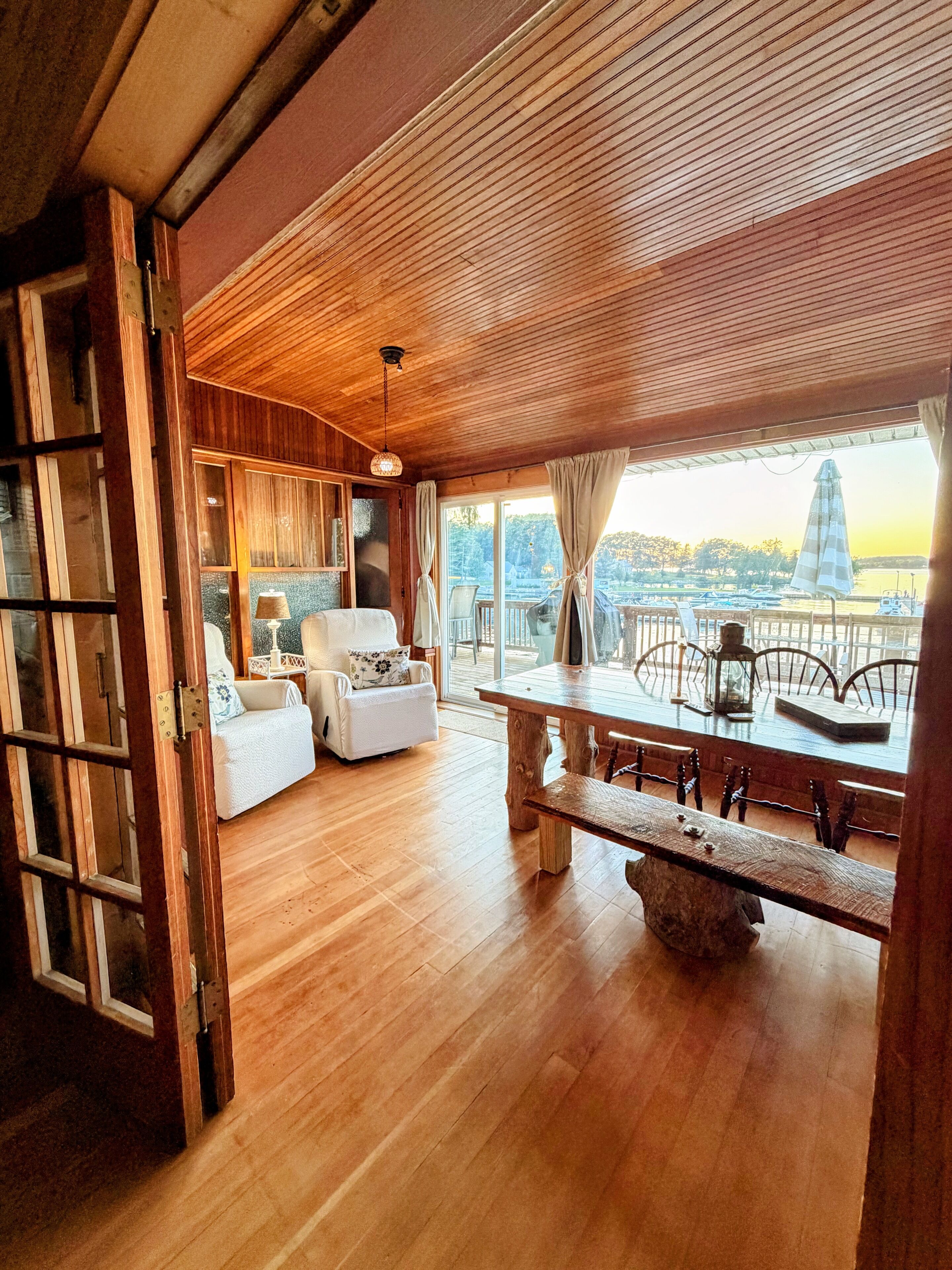 A wooden-floored room with a dining table and chairs, a sofa, and a view of the outdoors.