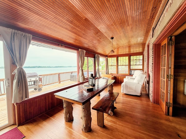 A wooden deck with a table and benches, a white chair, and a view of the water.