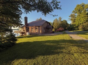 A brick house with a chimney, a deck, and a grassy yard.